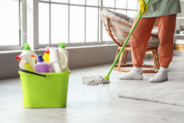 Woman with cleaning supplies in bucket mopping floor at home - obrazy, fototapety, plakaty