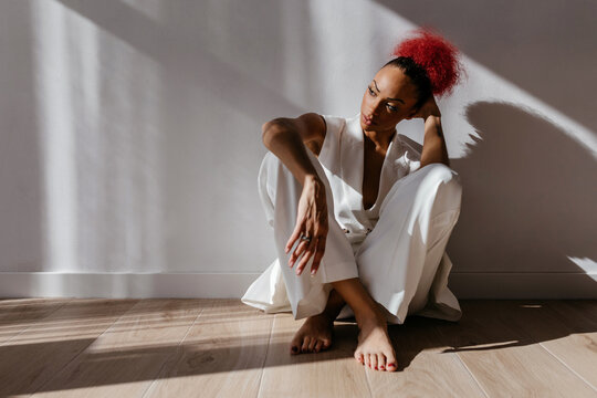 Thoughtful black woman sitting on floor in sunlight
