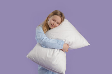Adorable girl in cozy pajamas hugging soft pillow on lilac background