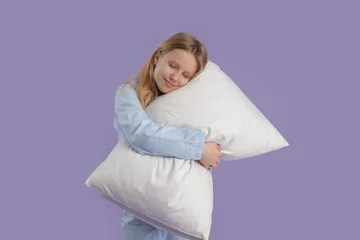 Gordijnen Adorable girl in cozy pajamas hugging soft pillow on lilac background © Pixel-Shot