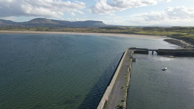 A drone shot over the pier, heading towards the Mullaghmore beach with Benbulben mountain in the background. County Sligo, Ireland.