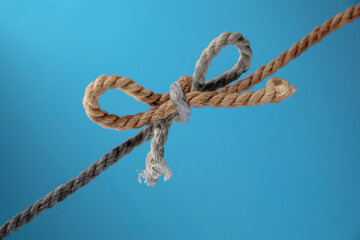 Two ropes, gray and brown, tied together in a bow, concept for teamwork and cohesion, blue background, copy space - 777744934