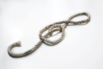 Old rough rope laying in the shape of a treble clef or violin key on a light gray background, musical symbol, copy space, selected focus - 777744955