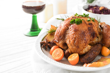 Festive poultry meal, roast chicken with kumquat, spices and herbs on a white table with red cabbage and wine, holiday dinner for two on Christmas or Thanksgiving, copy space