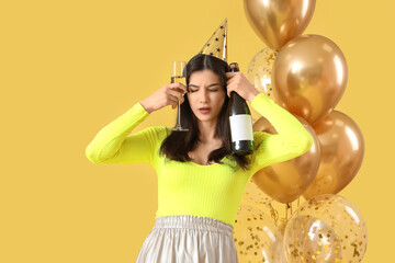 Young woman with hangover and champagne after Birthday party on yellow background