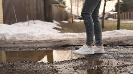 A woman in snow-white sneakers almost falls into a puddle. Stops in time and goes around her