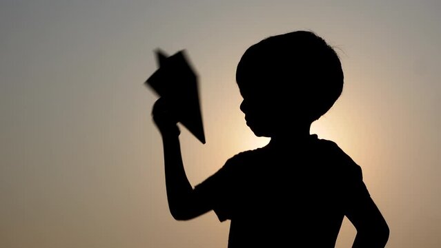 An Asian boy is playing with a paper plane in his hand at sunset. Concept of a boy's dream of becoming a pilot.