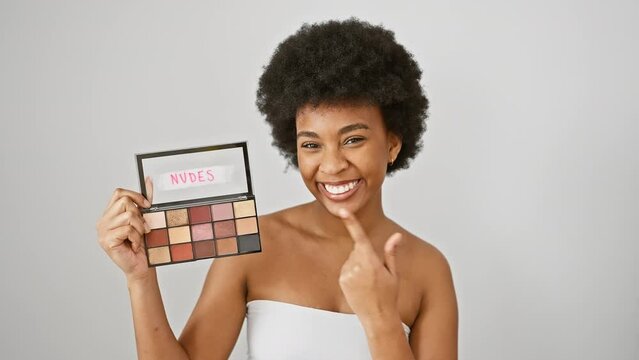 Cheerful african american woman excitedly pointing with her finger, holding makeup, smiling brightly isolated against a white background