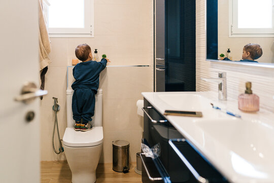 Anonymous child standing on toilet in bathroom at home