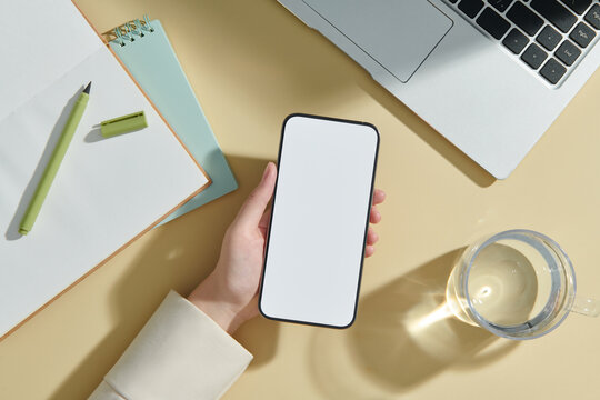 A woman is holding a smartphone on a working desk