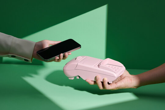 Hands holding pos device and smartphone on isolated color background