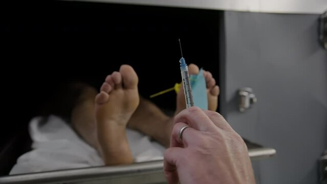 Doctor with embalming syringe in front of a morgue body