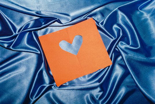 Valentine's Day red paper with heart shaped hole on blue satin