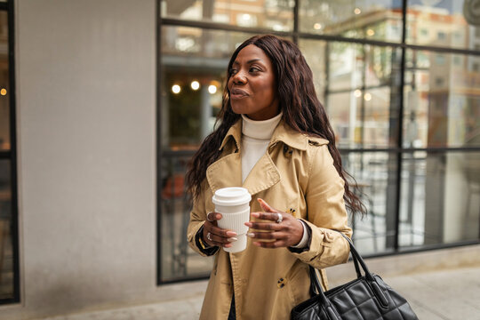 black woman walking through the city with a coffee in her hand