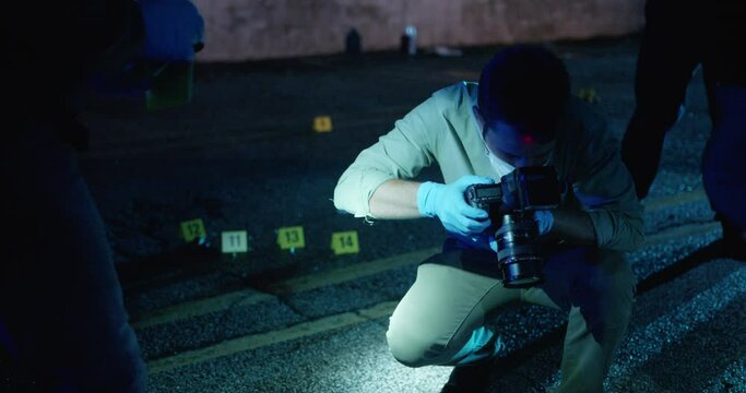 Police Forensic Photographer taking photos of Bullets and Blood at Crime Scene. Detectives walking around, Evidence Markers. Slow Motion.