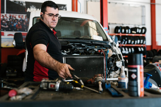 Male mechanic repairing vehicle in garage with screwdriver