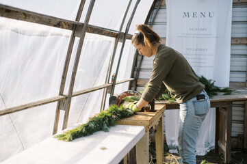 female farmer working with machine to tie pine garland in greenhouse