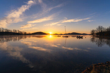 A spring peaceful sunrise with beautiful cloud reflections and silhouettes of boats. 