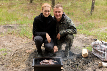 two people look at meat on fire. grill, picnic in the forest