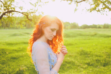 close-up of a woman in a blue dress with red hair and flowers in her hair, summer day for the concept of love and care. blue spring flowers in hands