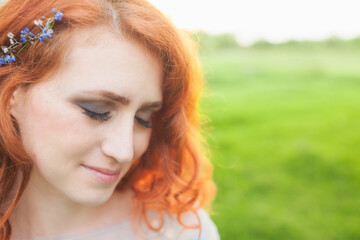 close-up of a woman in a blue dress with red hair and flowers in her hair, summer day for the concept of love and care. blue spring flowers in hands