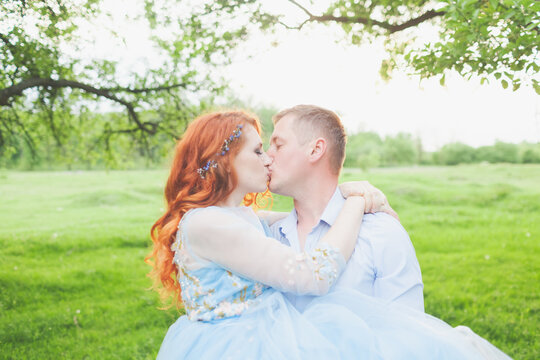 young couple in love kissing. woman with fiery hair in a blue dress. photo shoot in the garden