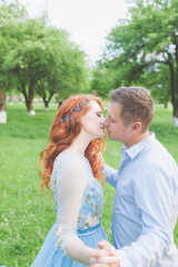 young couple in love kissing. woman with fiery hair in a blue dress. photo shoot in an apple orchard