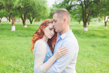 young couple in love hugging. woman with fiery hair in a blue dress. photo shoot in an apple orchard