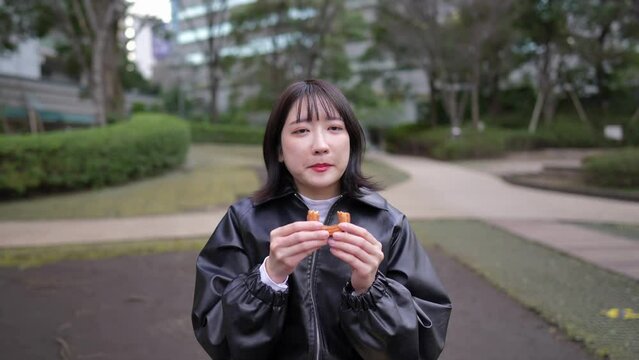 Slow motion video of a Japanese woman in her 20s eating donuts in a park around Gotanda Station in Shinagawa-ku, Tokyo in winter 冬の東京都品川区五反田の駅周辺の公園でドーナツを食べる20代の日本人女性のスローモーション映像