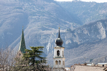 View of towers of church of Saints Peter and Paul (Chiesa dei Santi Pietro e Paolo) and Romanian Orthodox Parish of Trento. Dolomites mountains in the background; Trento city centre; Italy - obrazy, fototapety, plakaty