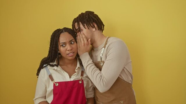 A woman and a man in aprons sharing a secret in a bright yellow indoor setting, capturing a moment of candid interaction.