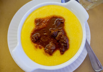 Traditional first course for lunch or dinner in Italy, yellow corn polenta porridge with stew served in Italian restaurant, Milan, Italy