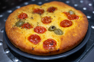 Tasty italian vegetarian food, fresh baked flat foccachia bread with cherry tomatoes, olives and herbs close up