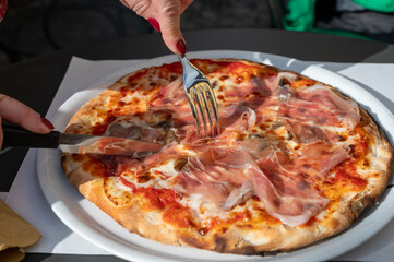 Eating of fresh baked pizza dish in italian pizzeria restaurant, Prosciutto di Parma