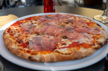 Eating of fresh baked pizza dish in italian pizzeria restaurant, Prosciutto di Parma