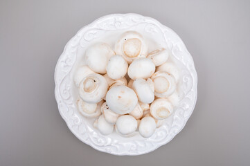White champignon mushrooms fresh uncooked on white ceramic plate copy space