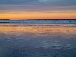 Sunset on Famara Beach, Lanzarote, casts a mesmerizing palette of colors across the sky, blending hues of orange, pink, and purple against the backdrop of the Atlantic Ocean waves.