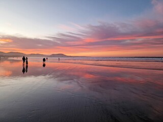 Sunset on Famara Beach, Lanzarote, casts a mesmerizing palette of colors across the sky, blending...