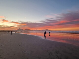Sunset on Famara Beach, Lanzarote, casts a mesmerizing palette of colors across the sky, blending hues of orange, pink, and purple against the backdrop of the Atlantic Ocean waves.