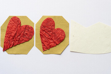 two hearts cut from textured paper on mustard colored paper polygons and creamy pastel paper piece...