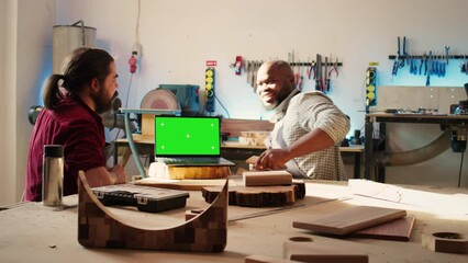 Upbeat men using CAD software on isolated screen laptop, debating wood design to use. Smiling cabinetmakers chatting, using program on chroma key notebook to make furniture schematics, camera B