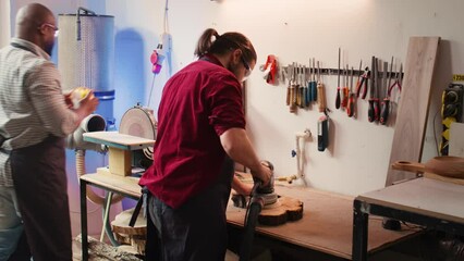 Craftsperson works with orbital sander with sandpaper on lumber to achieve smooth finish, checking quality. Woodworking expert in carpentry shop using angle grinder to fix wooden surface, camera B