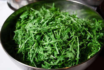 Fresh Arugula Leaves in a Stainless Steel Bowl. A bowl full of vibrant green arugula leaves, freshly washed and ready for salad preparation.
