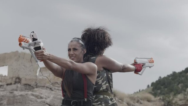 Cinematic shot of two women back to back with toy guns