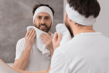 Washing face. Man with headband and towel near mirror in bathroom