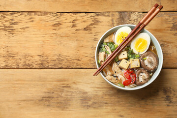 Bowl of delicious ramen and chopsticks on wooden table, top view with space for text. Noodle soup