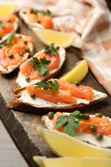 Tasty canapes with salmon, capers, lemon and cream cheese on wooden table, closeup