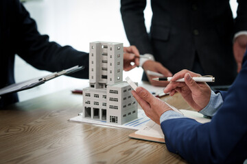 A professional businessman in a suit conducts a meeting at a desk while showcasing a model of a...