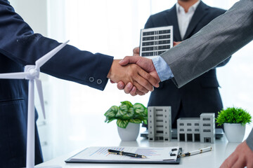 Two business professionals, both clad in suits, firmly shake hands, symbolizing mutual respect,...