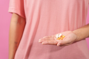 A professional image showcasing a female hand delicately holding a bottle of cod liver oil with her fingers against a soft pink isolated background.